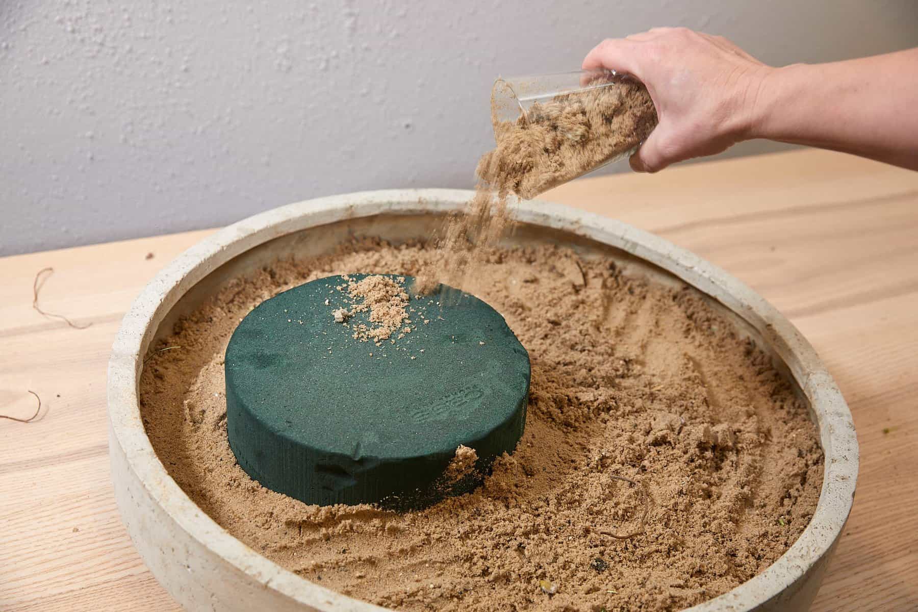 Steckschaum auf Sand wird mit Sand überschüttet