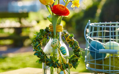 Buchsbaumkranz um Flasche mit Frühlingsblühern und kleinen Deko-Eiern