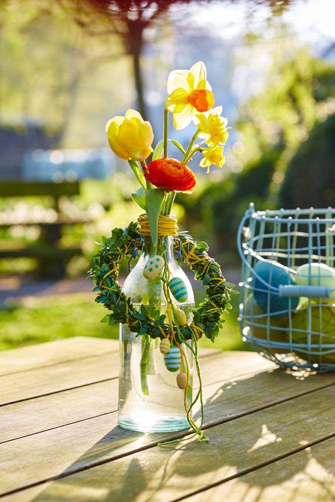 Buchsbaumkranz um Flasche mit Frühlingsblühern und kleinen Deko-Eiern