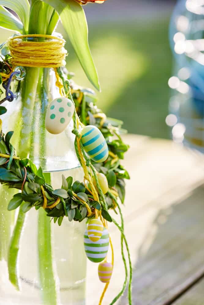 Close-up: Buchsbaumkranz um Flasche mit Frühlingsblühern und kleinen Deko-Eiern